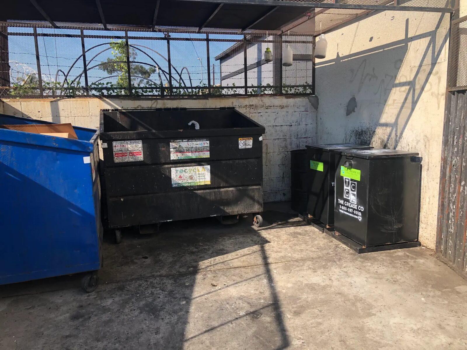 Used cooking oil bins and a drum inside a restaurant trash enclosure for cooking oil disposal in Fullerton, California